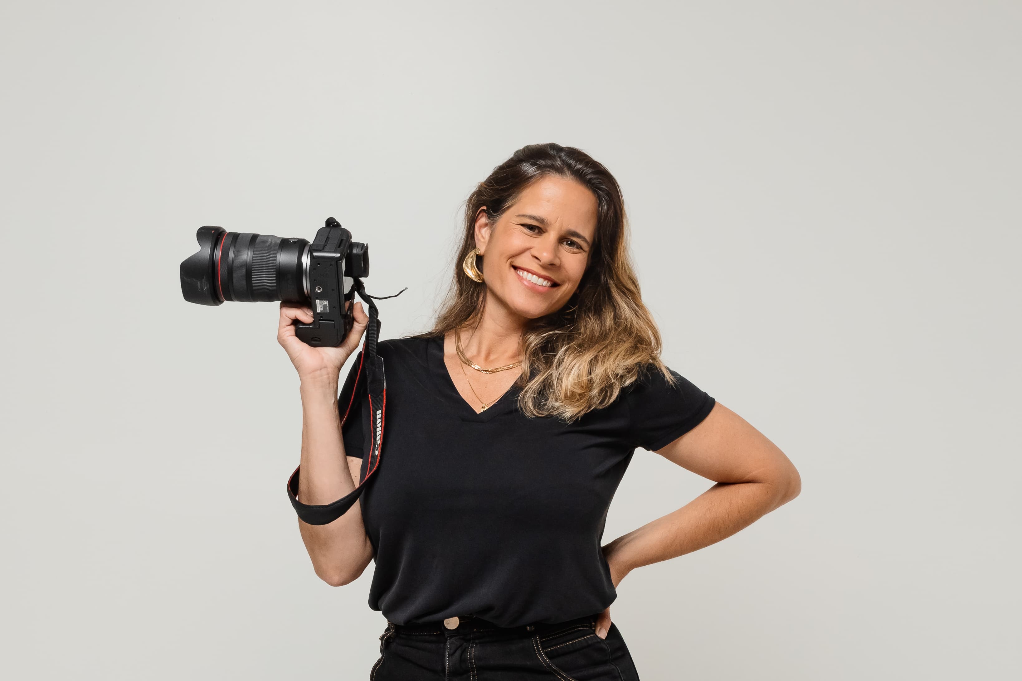 Fotógrafa vestida de preto num cenário fotográfico posando com uma câmera profissional na mão